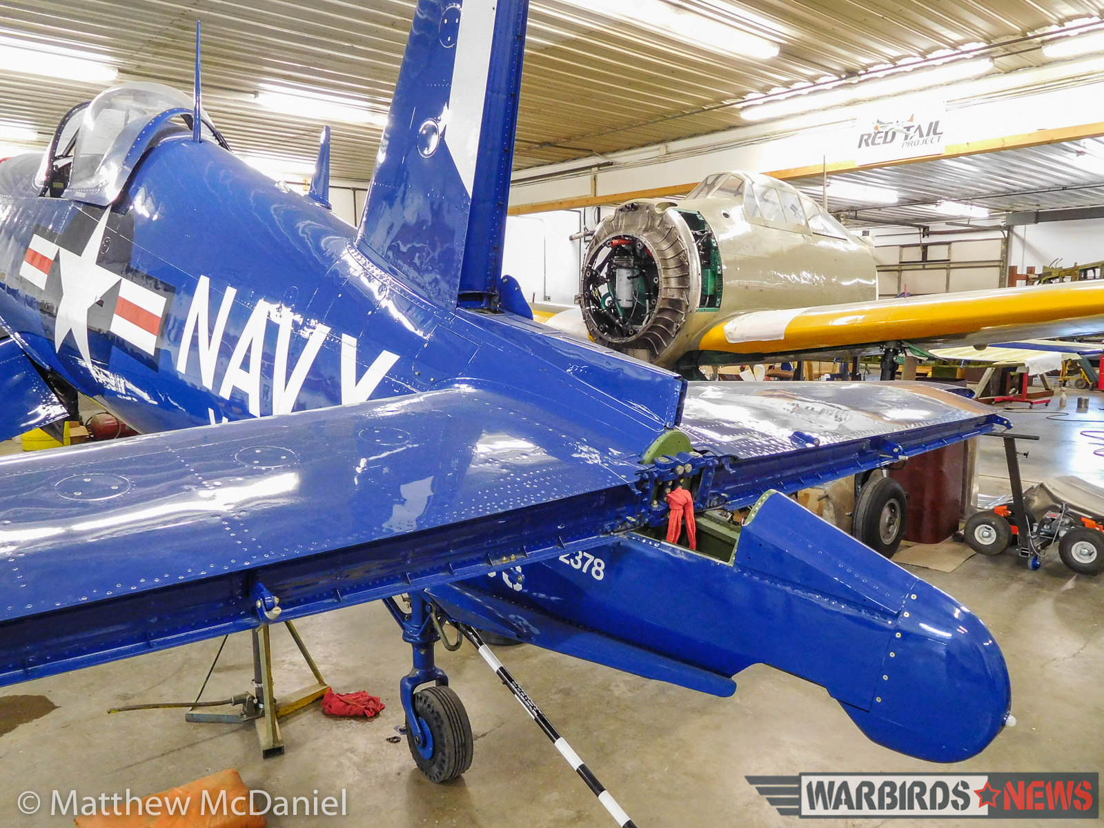 The F4U-4 Corsair and its former Pacific Theater foe, the A6M2 Zero, share close quarters inside the Tri-State aviation main hangar-shop, both entering the final stages of their repair programs back to airworthy status. (photo by Matthew McDaniel)