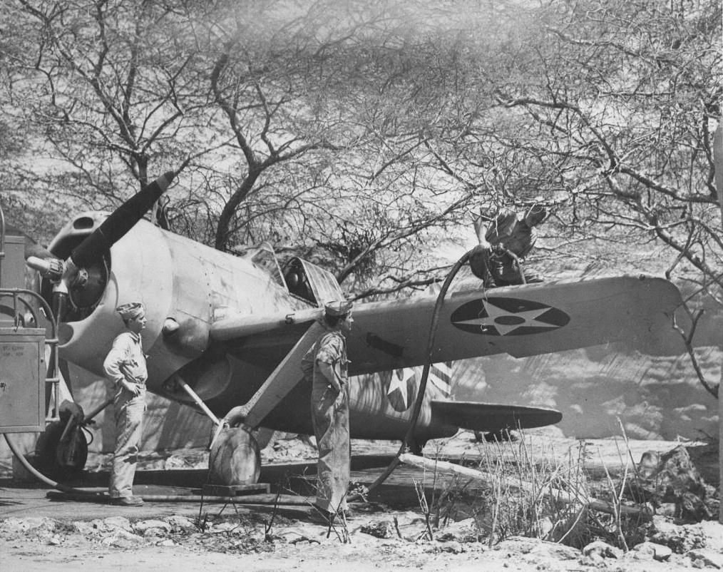 A Brewster F2A Buffalo being refueling at Ewa in May, 1942. Note the attempt to hide the aircraft under the thorny Kiawe trees and the sandbag revetment in the background.