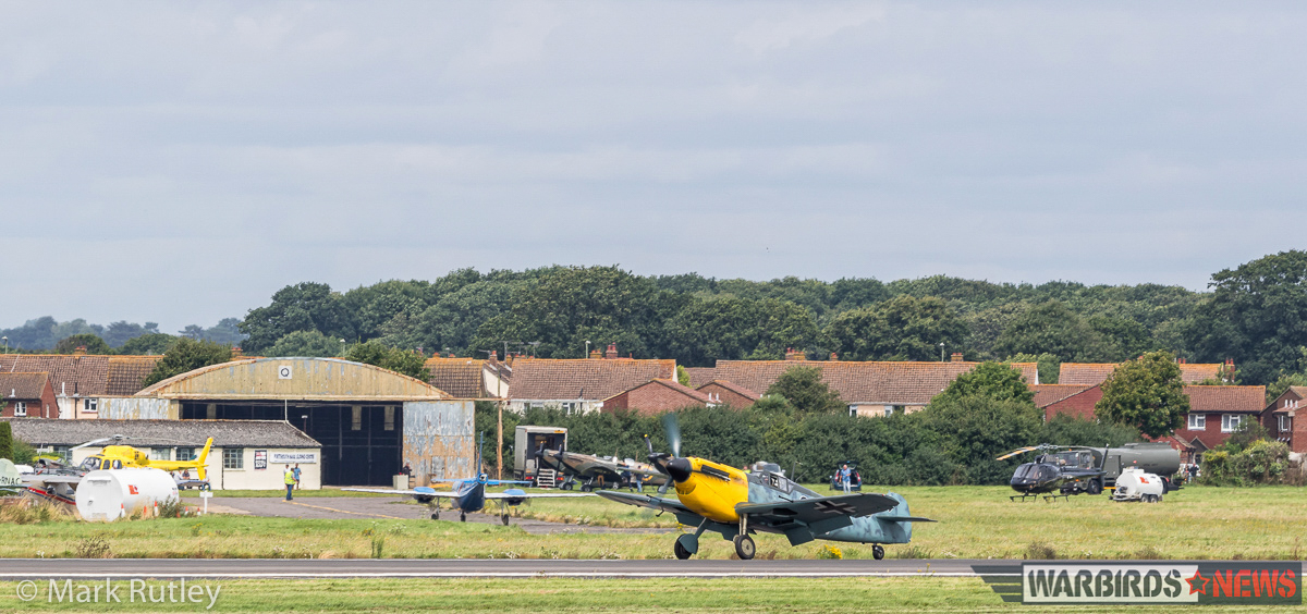 The Buchon, masquerading as its older sibling, the Me 109, taxiing for take off at Lee on Solent while a brace of Spitfires sit idly on the tarmac behind. (photo by Mark Rutley)